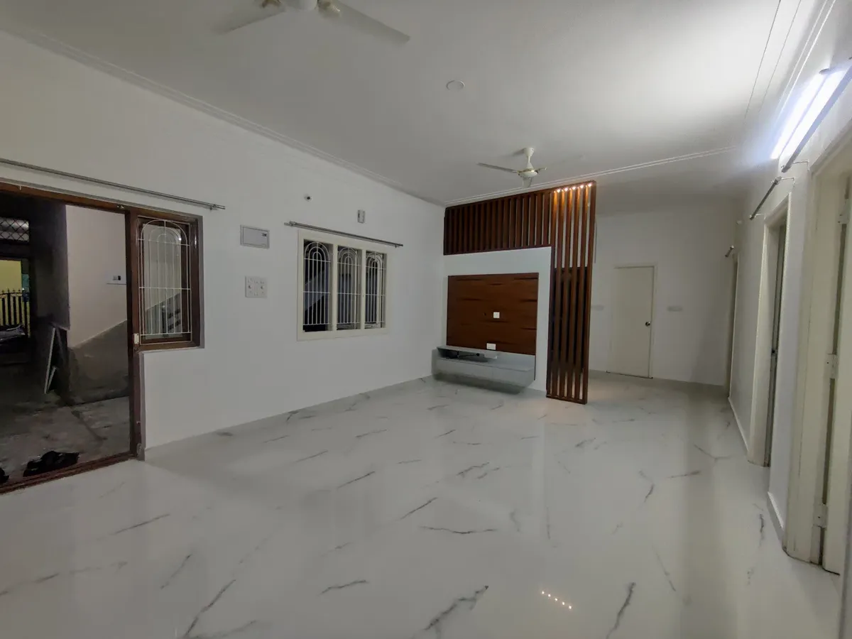 Empty living room with white marble flooring, a wood-slat partition screen beside a wood-panelled TV wall, and a grilled window