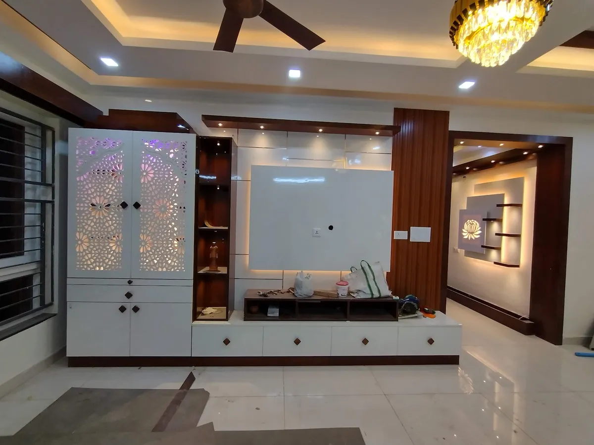 Handover-stage living room where a white TV unit runs into a backlit CNC floral-jaali pooja cabinet