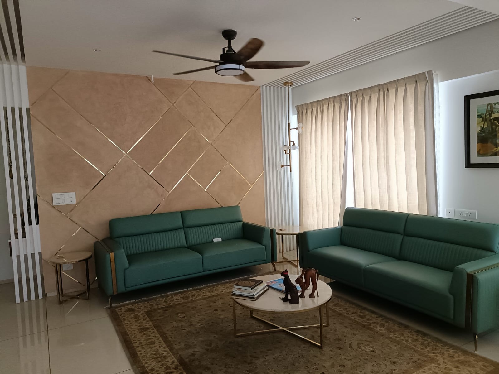 Two emerald green leather sofas facing a marble-and-gold coffee table, set against a peach diamond-quilted accent wall with brass inlay strips.