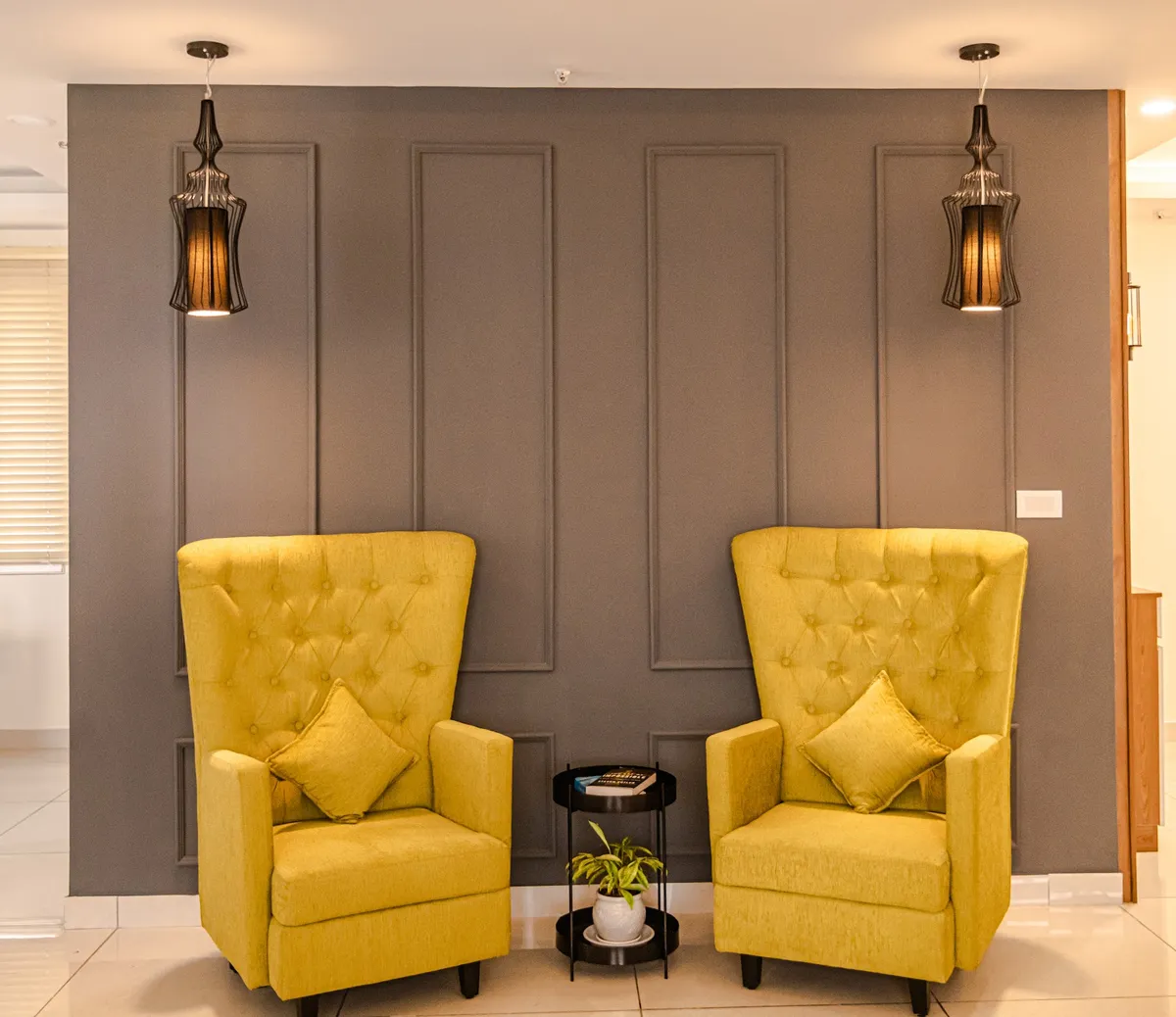 Symmetrical living-room vignette: two mustard button-tufted high-back wing chairs flanking a small black two-tier round table