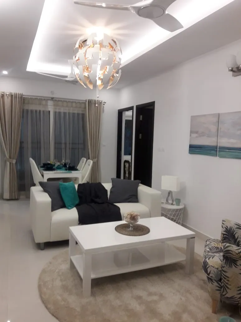 Open-plan living-dining space with a sculptural white pendant light, a cream sofa with teal and charcoal cushions, and ocean-themed wall art