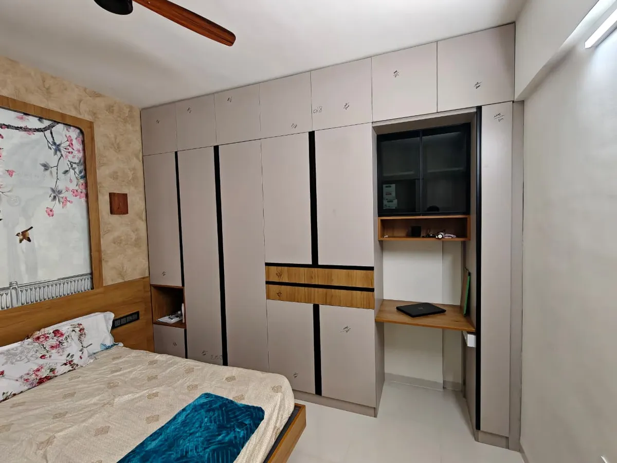 Greige wardrobe run banded with black grooves and teak strips, wrapping into a built-in study niche with a tinted-glass overhead unit