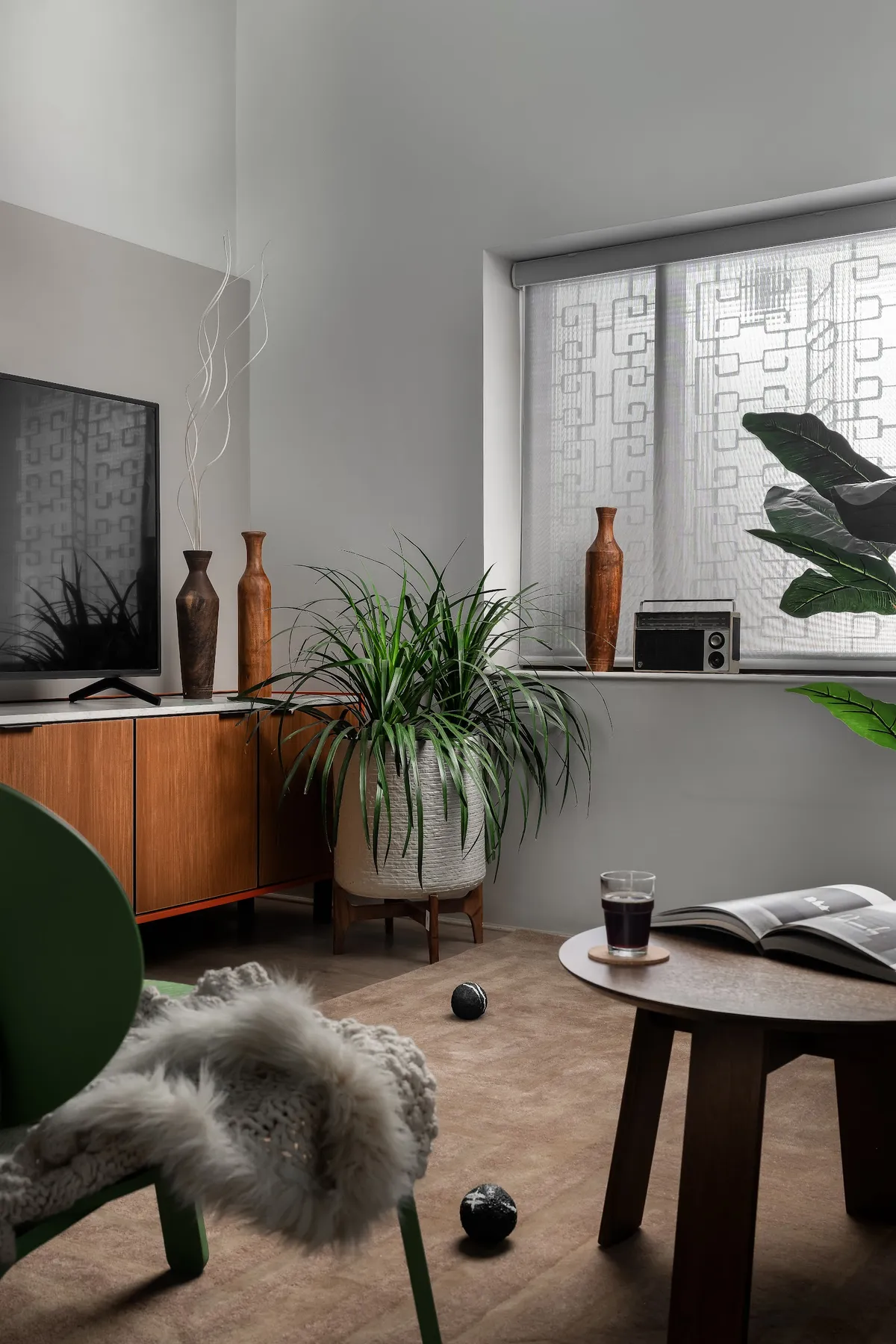 Living-room corner where a teak sideboard on an orange plinth carries the TV beside turned wooden vases and a vintage transistor radio