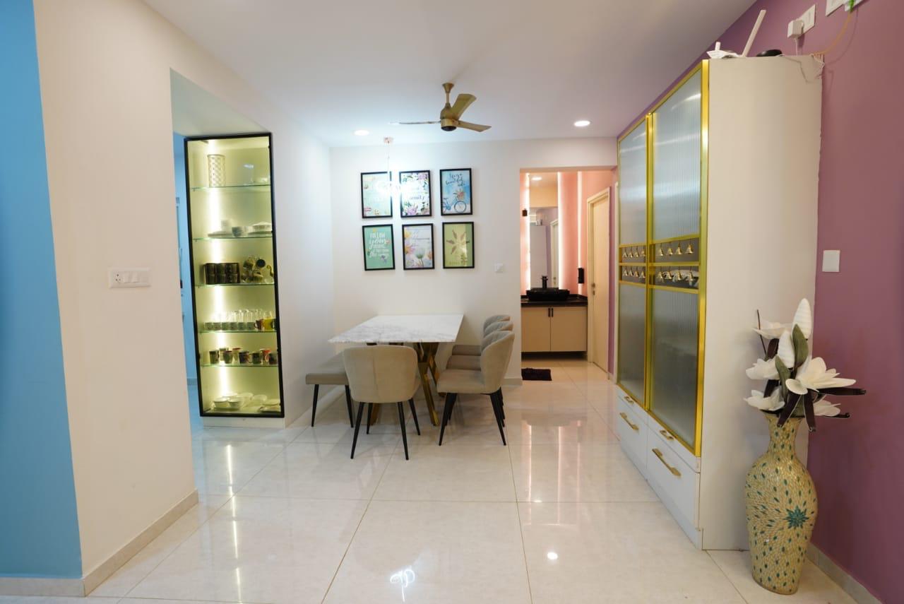 Dining area with a marble-top table and upholstered chairs, a backlit glass crockery display cabinet, a framed gallery wall