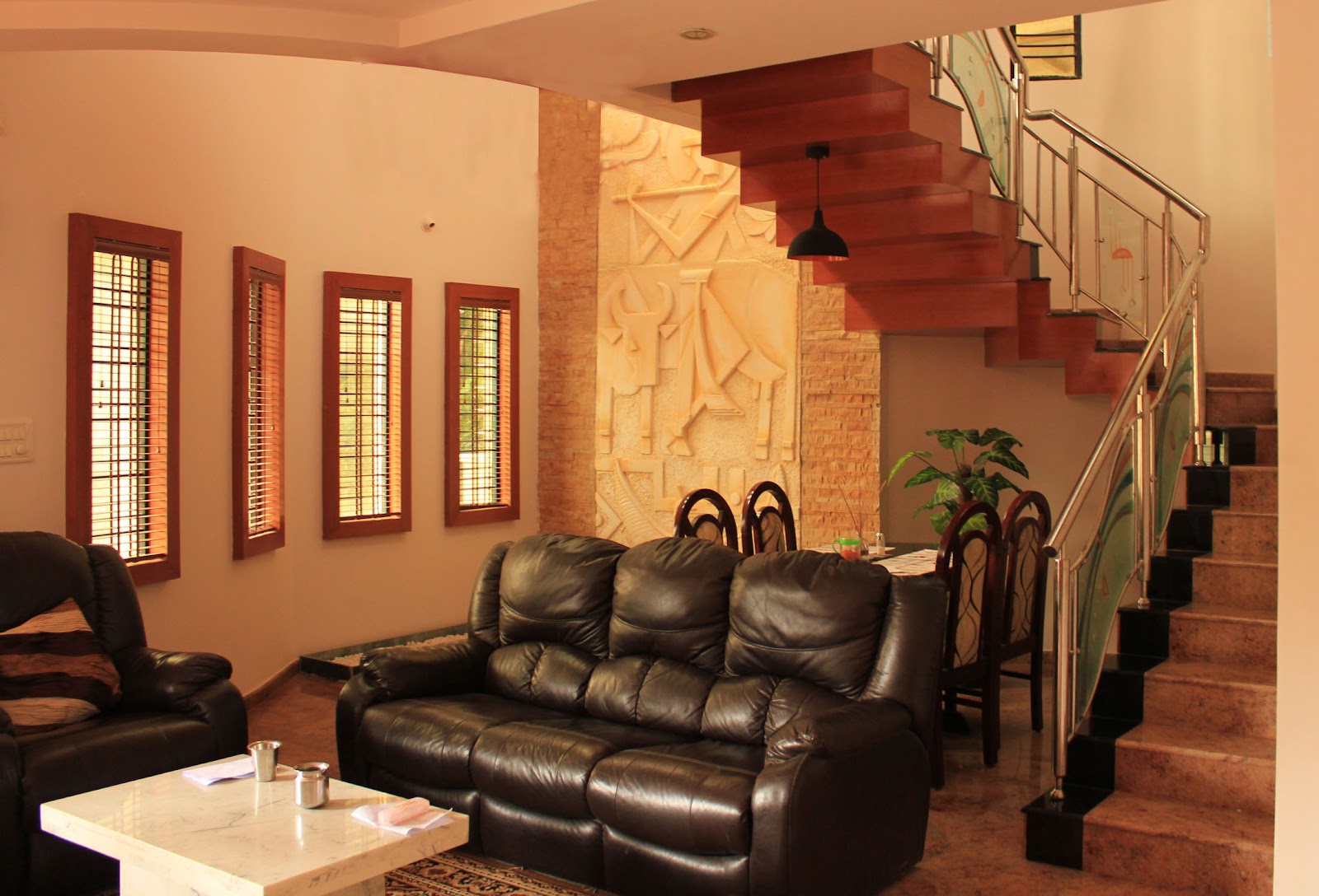 Living room with a black leather reclining sofa set, a marble coffee table, and a carved stone relief mural wall beneath the staircase.