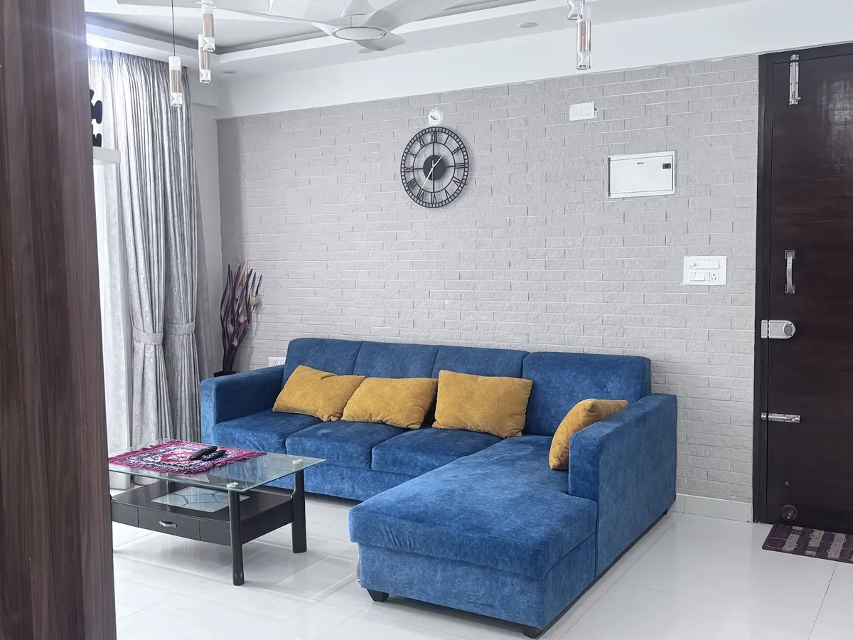 Denim-blue L-shaped fabric sofa with mustard cushions against a whitewashed brick-tile wall
