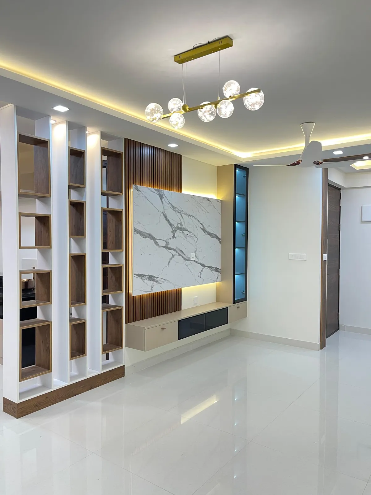 Newly handed-over living room, still unfurnished: a marble-look laminate TV back panel framed by walnut fluted strips, a slim backlit glass display column