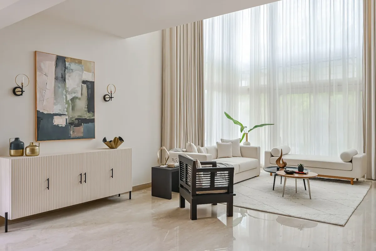 Double-height living room with a fluted white console under an abstract painting, a black wood armchair, cream sofa