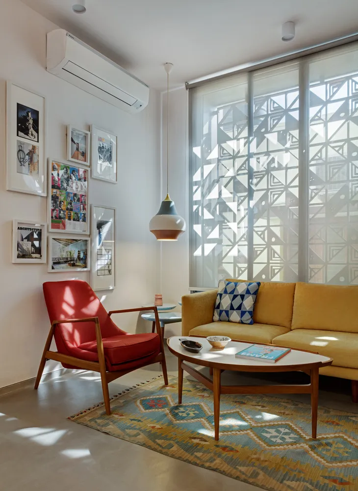 Late afternoon sun striping a mustard three-seater and a red-cushioned teak armchair over a blue-and-ochre kilim