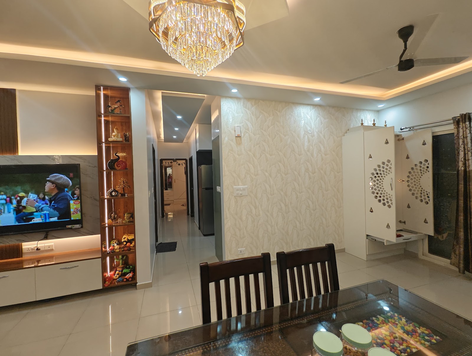 Open-plan living-dining space with a wood display shelf beside the TV unit, a dining table in the foreground