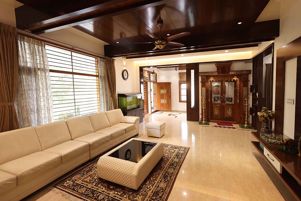 Living room with a dark wood beamed ceiling and pendant fan, a cream leather sectional sofa, a patterned area rug and glass-top coffee table