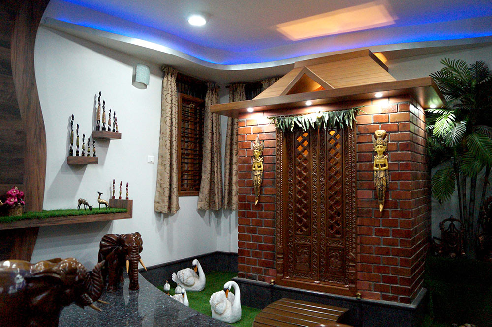 Pooja room with an exposed-brick temple facade and carved wood doors, cove-lit in blue
