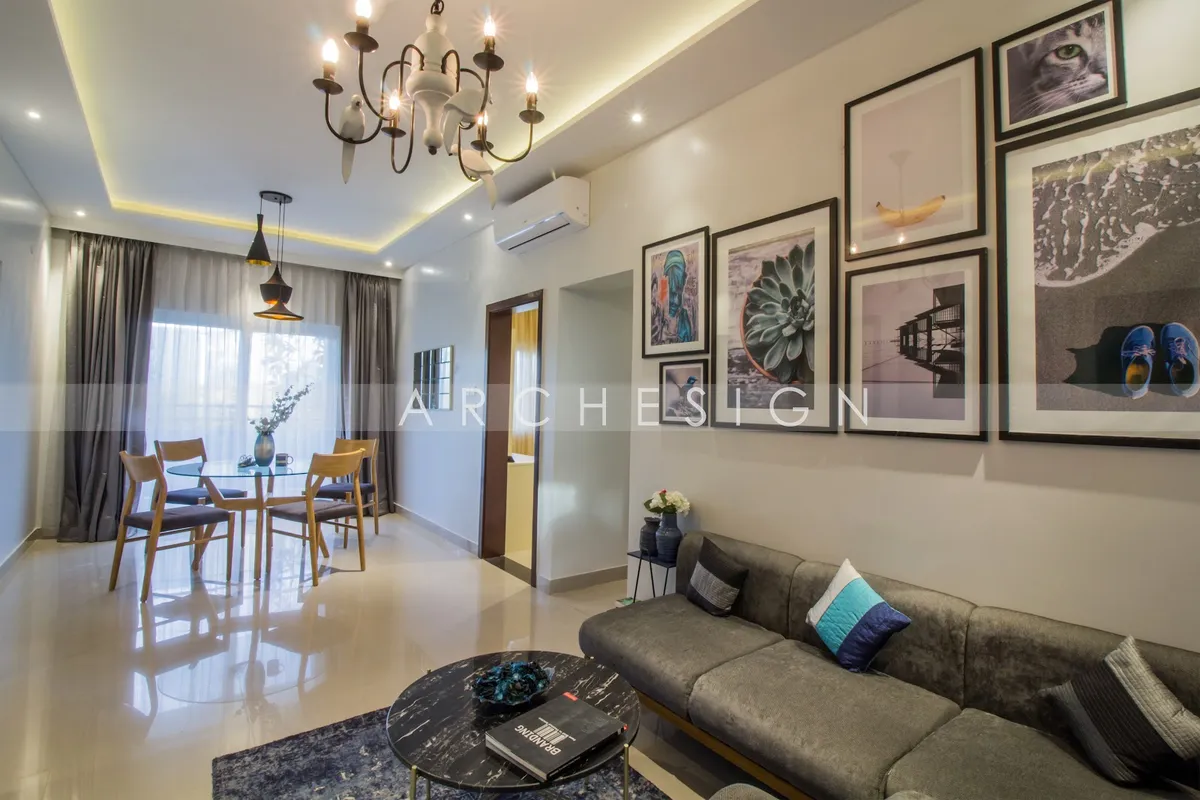 Open living-dining where an olive-grey L-sofa sits under a nine-frame gallery wall of photo prints, a black marble round table on a blue rug in front of it