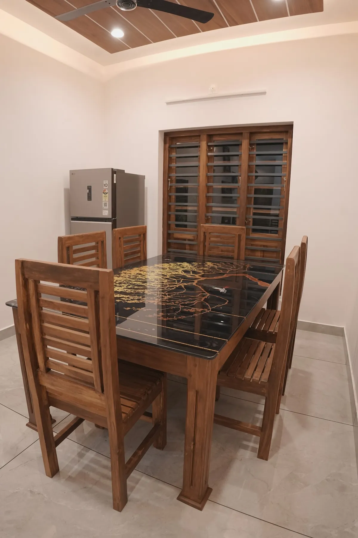 Dining room with a solid teak six-seater whose black glass top is hand-painted with a golden tree and a bird, slatted-back teak chairs around it
