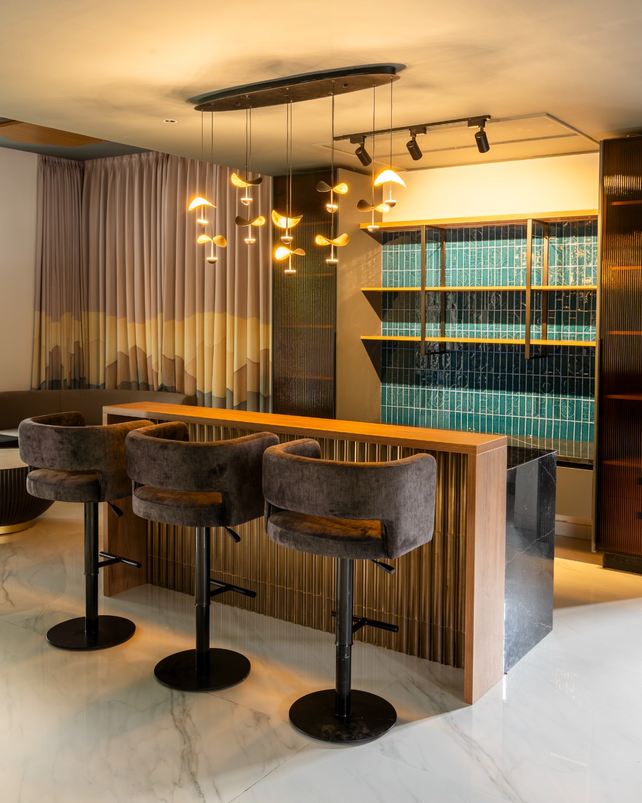 Home bar nook with a fluted-wood and brass counter topped in black marble, velvet swivel bar stools, a sculptural cluster pendant light