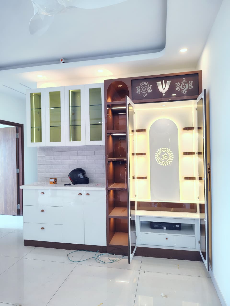 Built-in pooja unit with a backlit arched niche and an Om-motif frosted glass panel, open temple doors