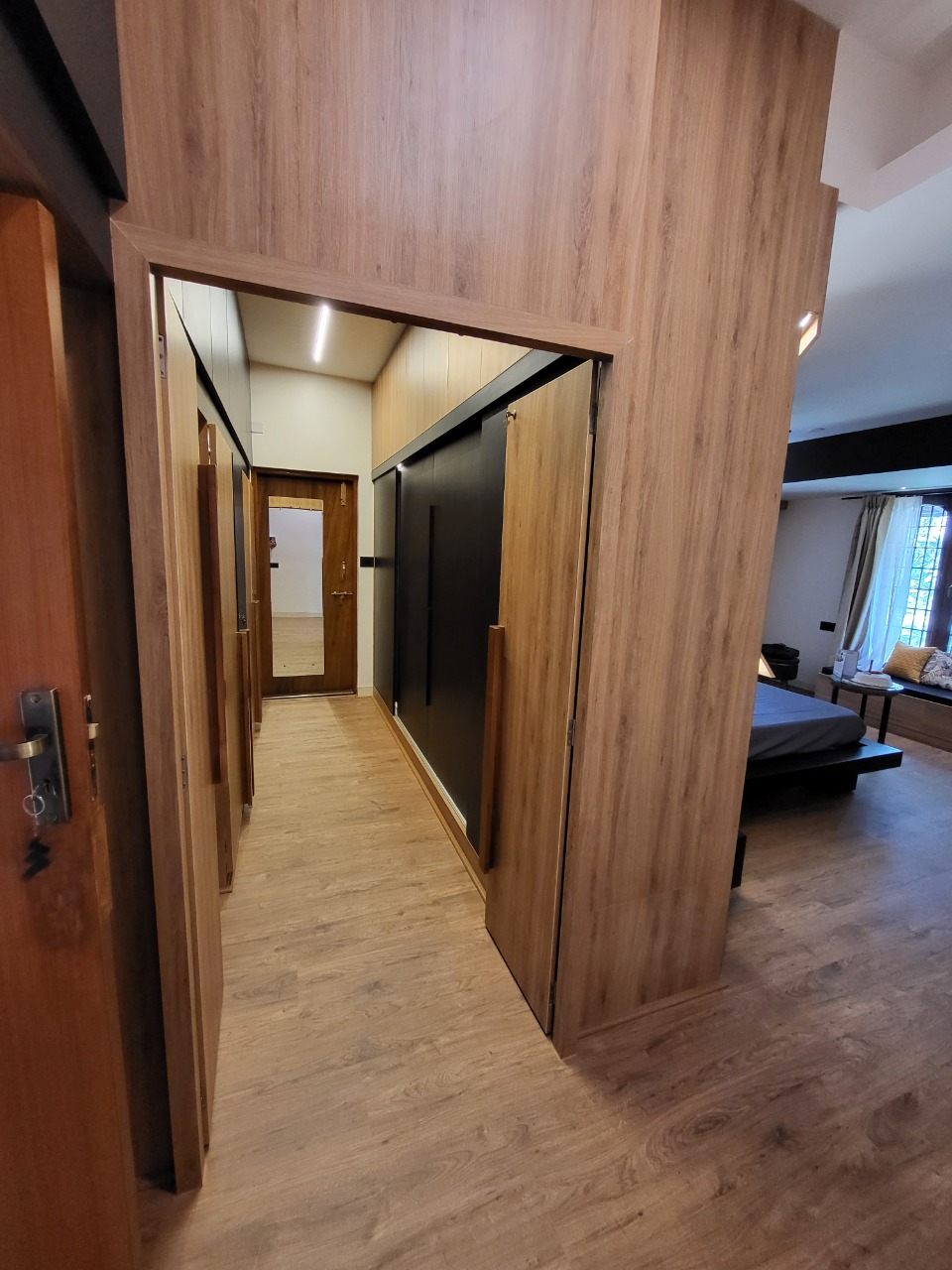 Bedroom suite with a wood-panelled walk-in wardrobe passage leading to the bed and a window seat bench.