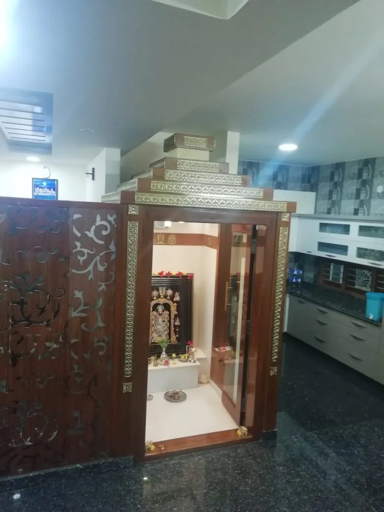 Dedicated pooja room with a tiered gold-trimmed wooden temple mandir and a carved wood jaali screen room divider, deity idols placed inside.