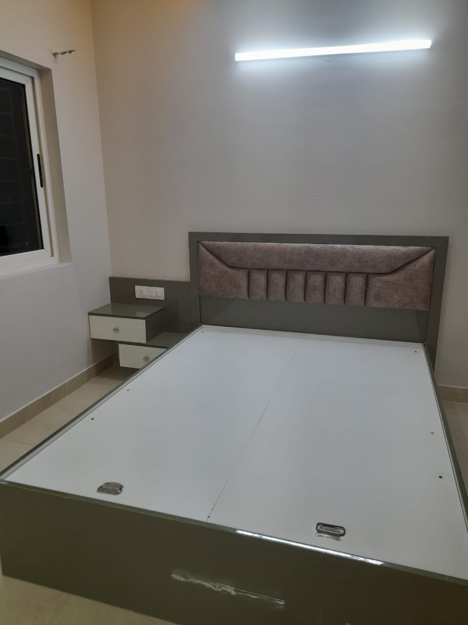 Bedroom with a grey laminate storage bed featuring a channel-tufted mauve upholstered headboard, and a matching wall-mounted bedside table with two drawers