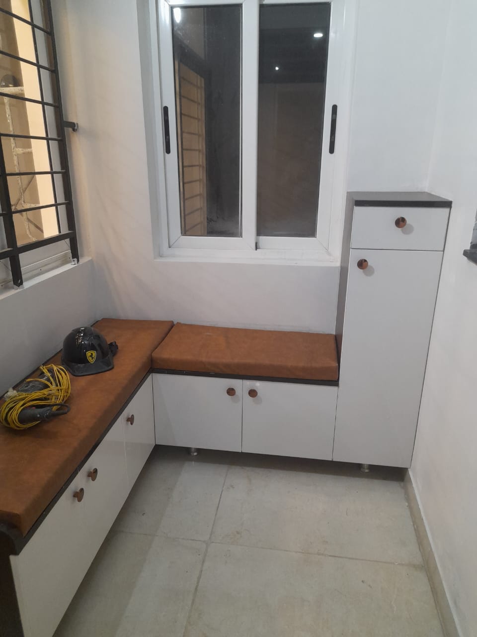 Balcony utility nook with an L-shaped white storage bench topped in tan leatherette cushions and a tall matching storage cabinet