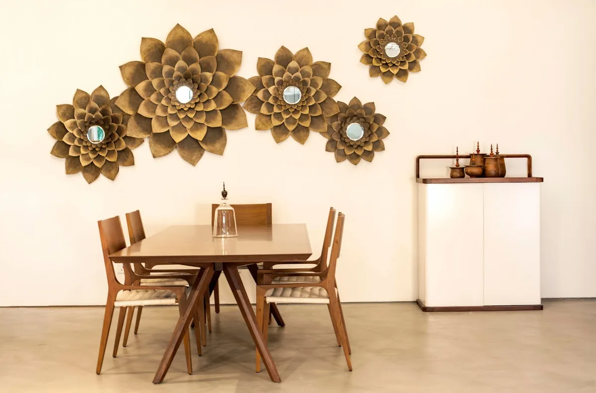 Dining corner with a teak table on splayed compass legs and cane-seat chairs, under a staggered cluster of brass lotus discs with mirrored centres