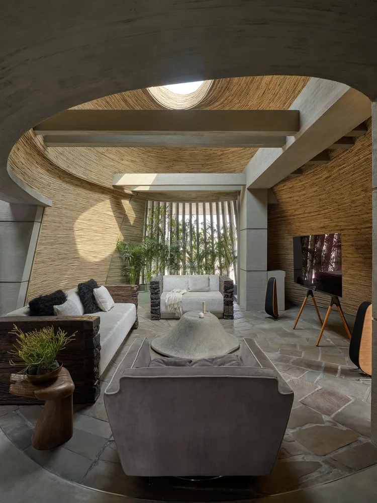 Living room with a sculptural reed-clad concrete ceiling, an oculus skylight, sheepskin-trimmed sofas, a raw-stone coffee table
