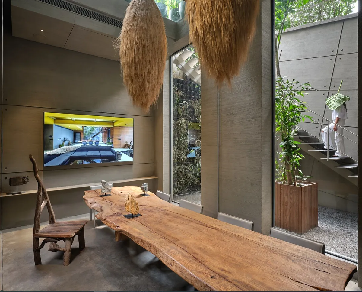 Double-height dining space with a live-edge wood slab table, a driftwood-frame chair and hanging dried pampas grass