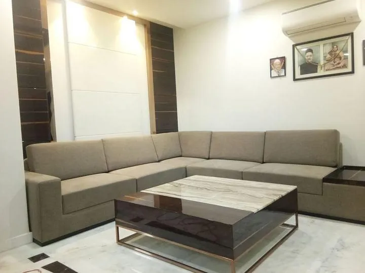 A living room with a beige L-shaped sectional sofa and a marble-top coffee table with brass trim, set against a dark wood and light-panel accent wall.
