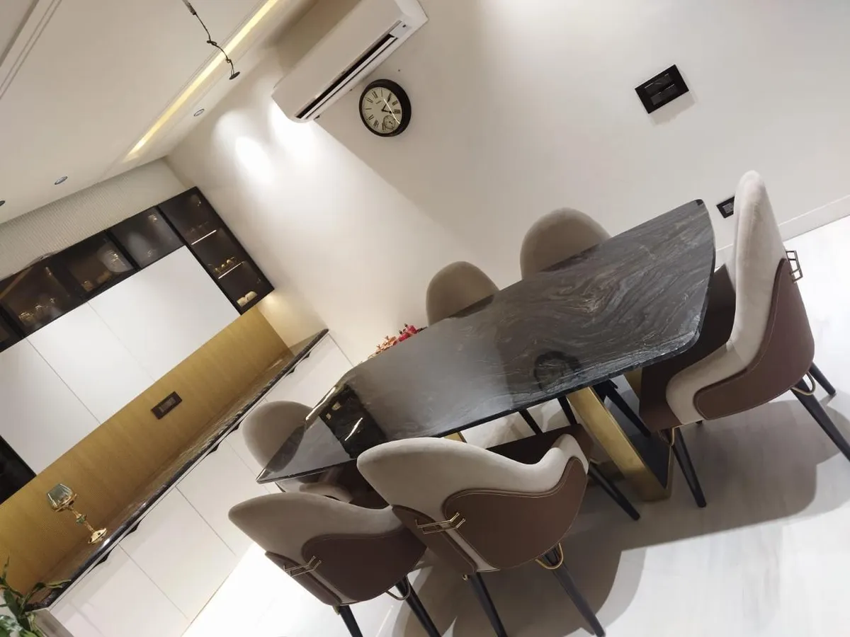 Dining room with a live-edge black stone slab table on a gold pedestal base, two-tone tan-and-brown upholstered chairs