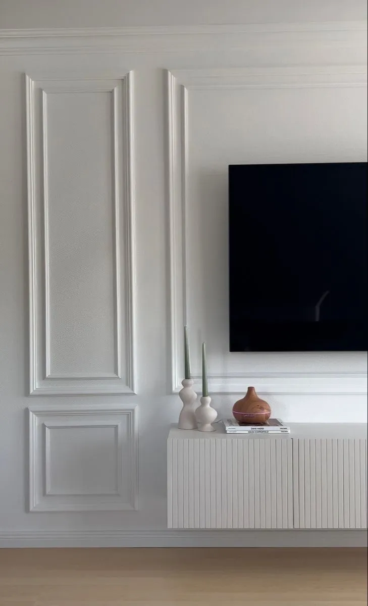 Living room TV wall with tall white panel moulding, a fluted floating TV console styled with ceramic vases, candles, and stacked books