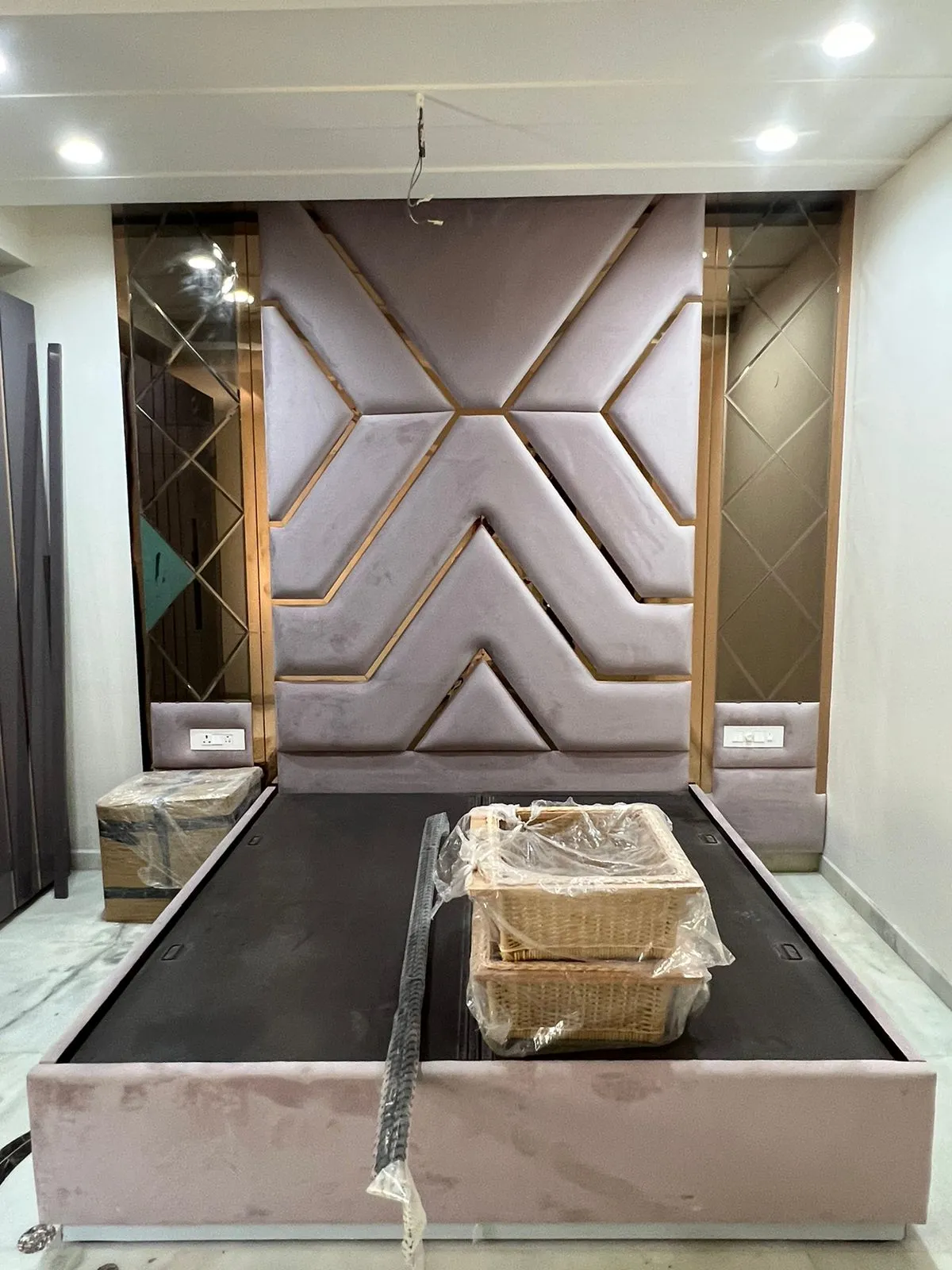Blush velvet headboard wall cut into a chevron pattern with rose-gold inlay strips, bronze bevelled mirror bays either side