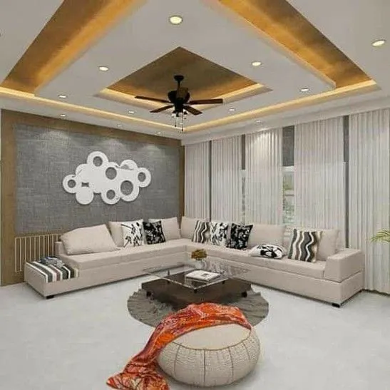 Living room with a stepped gold-cove POP ceiling, a grey textured accent wall with a circular mirror art piece, and a beige L-shaped sectional.