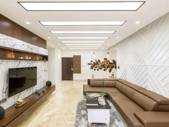Living room with a book-matched white marble TV wall framed in walnut, a tan leather L-sofa on a grey shag rug
