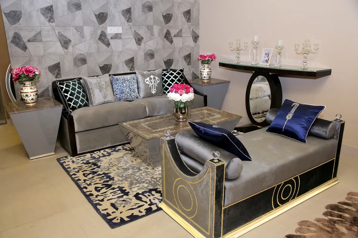 Grey velvet sofa piled with embroidered and navy cushions beside a gold-trimmed velvet chaise with crystal finials, around a brass-inlay coffee table