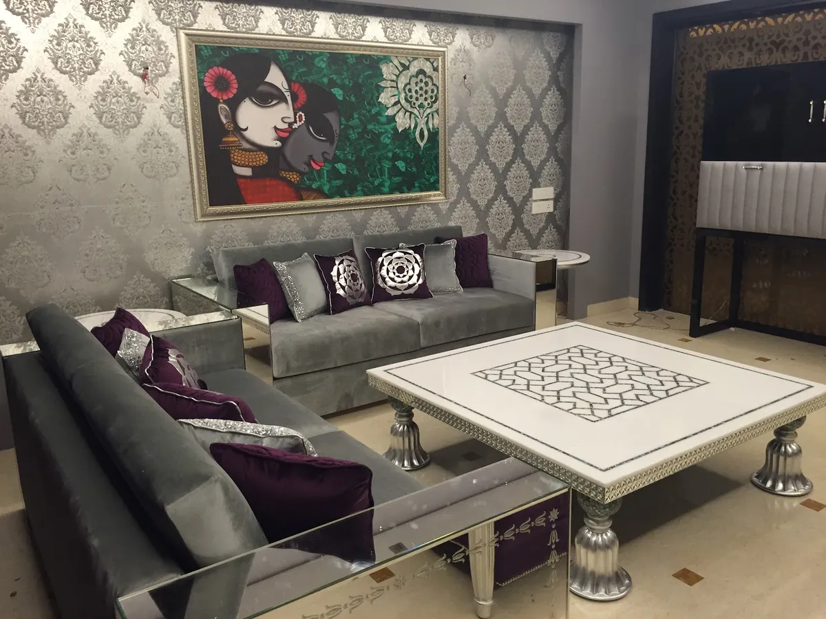 Grey velvet sofas with aubergine and sequinned silver cushions set against silver damask wallpaper, under a framed Radha-Krishna painting