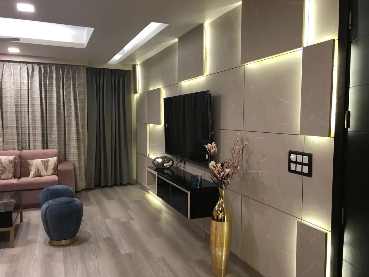 Living room where a staggered beige stone-effect panel wall is lit by strips hidden in its setbacks, with a black floating TV console