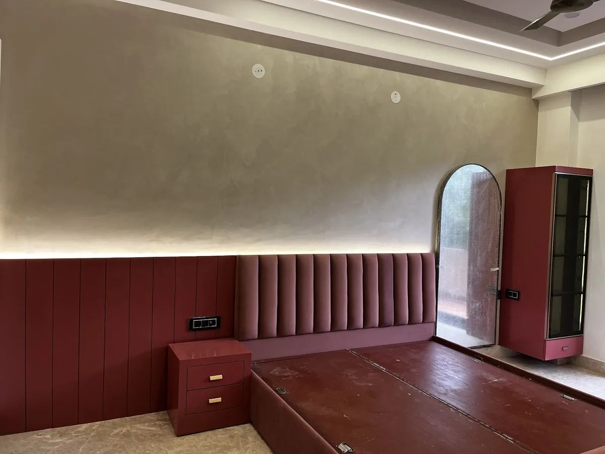 Bedroom still being handed over - a channel-tufted wine velvet headboard runs the length of the wall over a maroon vertical panelled dado