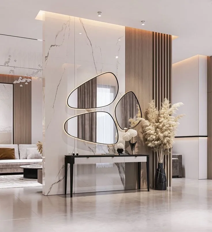 Render of an entry foyer built around a full-height veined marble partition carrying three organic pebble-shaped backlit mirrors, with a slim black console