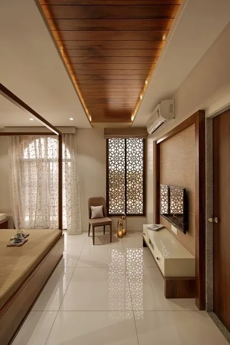 Bedroom looking down a wood-planked ceiling raft edged in cove light to a white CNC jaali screen across the window