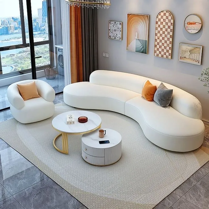 A living room with a curved white sectional sofa and matching armchair, round marble-top coffee tables, and a curated gallery wall.
