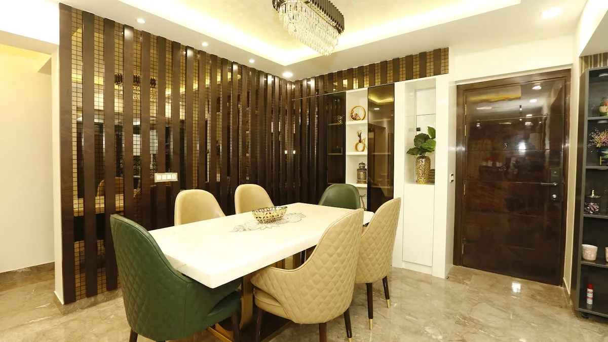 Dining area screened by a dark-wood vertical fin wall inset with bronze mirror strips, a white marble-top six-seater with green and beige quilted chairs