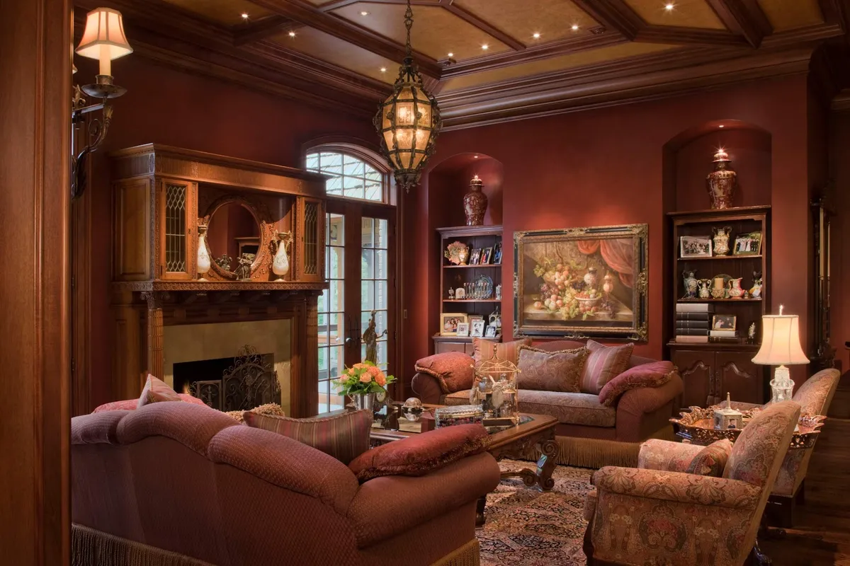 Classic living room with deep red walls, a coffered wood beam ceiling, an ornate lantern chandelier, a carved stone fireplace with mirrored overmantel