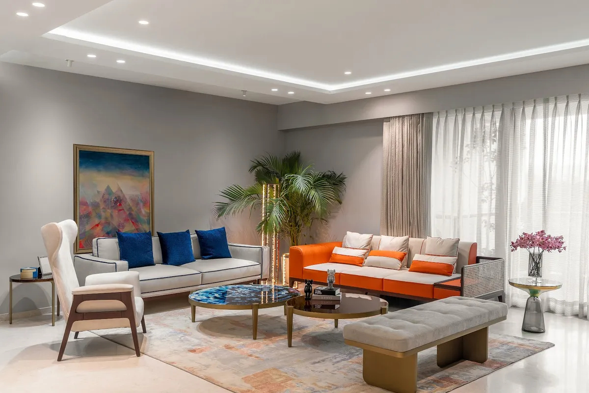Living room with an orange velvet sofa and a cream wingback armchair around twin marble-top coffee tables, navy accent pillows