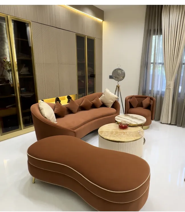 Curved rust velvet sofa with a peanut-shaped bench in front of it, round marble and fluted side tables between