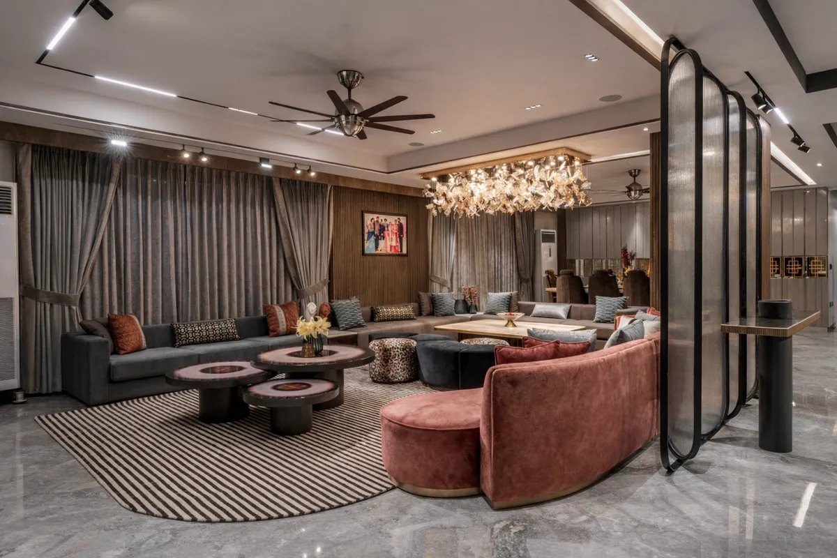Long charcoal sofa run and a curved rose-velvet sofa on a black-and-cream striped rug, around a cluster of round two-tone coffee tables