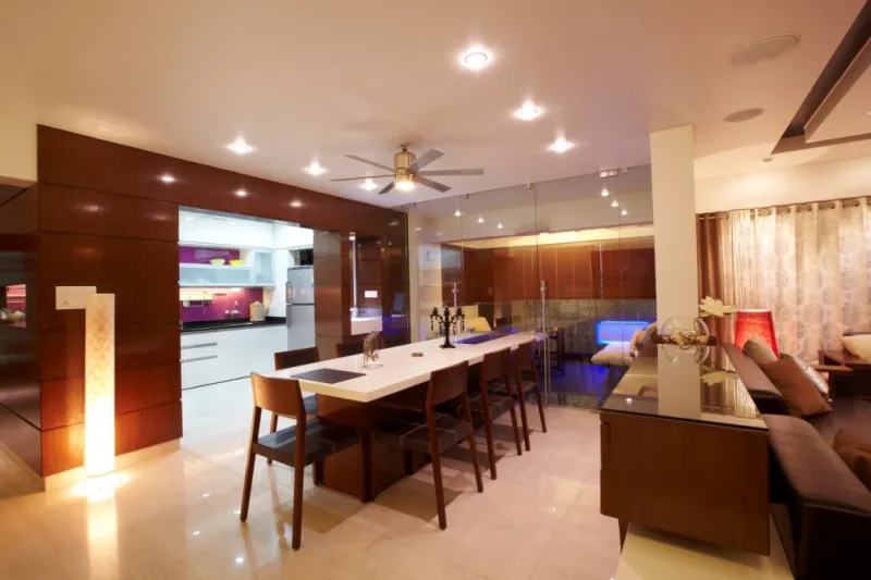 An open-plan space showing a wood-panelled dining area, a compact galley kitchen, and a leather sofa lounge with a glass-partitioned feature nook