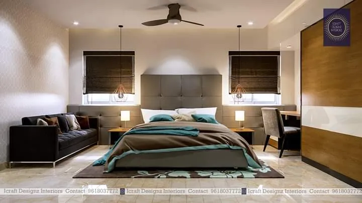 Bedroom with a tall grey channel-tufted headboard, teal-and-brown bedding, twin pendant bedside lights, and a dark tufted bench sofa at the foot of the bed.