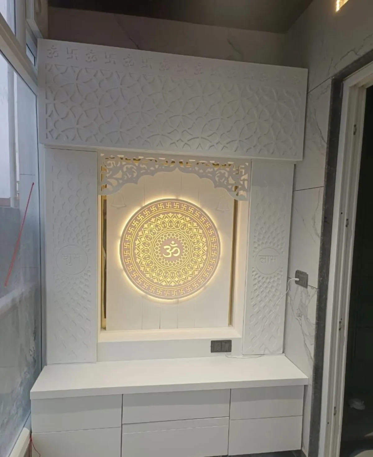 All-white CNC pooja unit with a Swastik-bordered backlit Om mandala, Shubh-Labh carved side panels and a drawer base