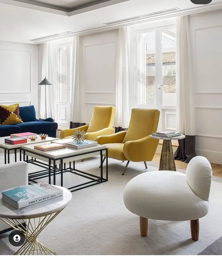Bright panelled living room with a pair of mustard velvet lounge chairs on brass legs set between two French windows, a navy sofa along the left wall