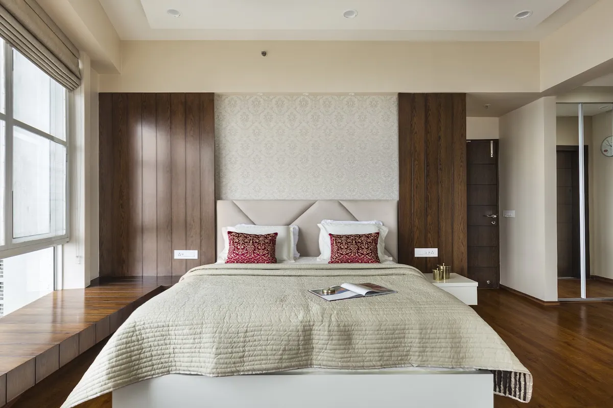 Bedroom with a damask wallpaper panel above an upholstered geometric headboard, flanked by dark walnut vertical-groove panelling and a mirrored sliding